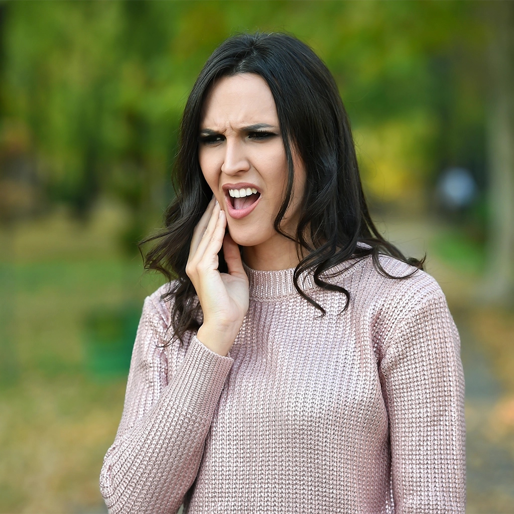 woman touching cheek with tooth pain in the outdoors